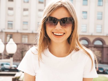 Yaz hipster giysileri giymiş güzel gülümseyen sarışın model portresi. Sokak arka planda poz veren modaya uygun bir kız. Güneş gözlüğü komik ve pozitif kadın