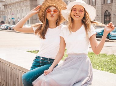 Moda yaz beyaz t-shirt giysiler iki genç güzel sarışın gülümseyen hipster kız Portresi. Seksi kaygısız kadınlar sokak arka planda poz. Güneş gözlüğü ve şapka ile eğlenen pozitif modeller