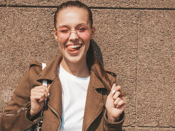 Portrait of beautiful smiling brunette model dressed in summer hipster jacket and jeans clothes. Trendy girl posing in the street near wall. Funny and positive woman. Winking