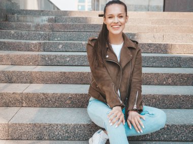 Yaz hipster ceket ve kot elbise giymiş güzel gülümseyen esmer model Portresi. Sokak arka planda merdivenlerde oturan trendy kız. Yuvarlak güneş gözlüğü komik ve pozitif kadın