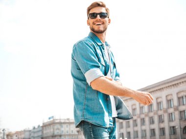 Yakışıklı gülümseyen şık hipster lumbersexual işadamı modeli portresi. Kot pantolon ceketi giymiş bir adam. Moda erkek güneş gözlüğü sokak arka planda poz