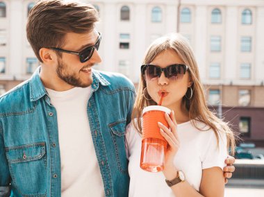 Gülümseyen güzel kız ve rahat yazlık giysiler onun yakışıklı erkek arkadaşı. Mutlu neşeli aile sokak arka planda eğlenmek. Güneş gözlüğü yle. Saman ile şişeden kadın içme suyu