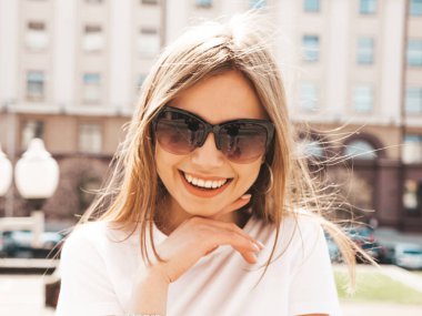 Yaz hipster giysileri giymiş güzel gülümseyen sarışın model portresi. Sokak arka planda poz veren modaya uygun bir kız. Güneş gözlüğü komik ve pozitif kadın