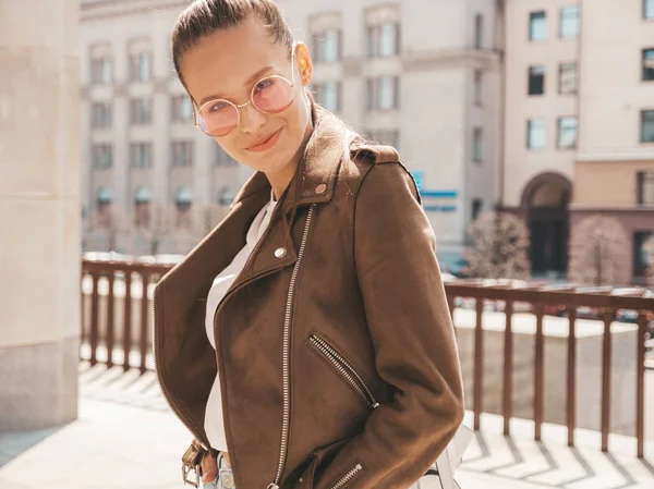 Portrait of beautiful brunette model dressed in summer hipster jacket clothes. Trendy girl posing in the street background. Funny and positive woman in round sunglasses