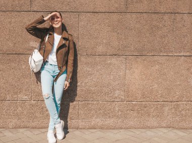 Yaz hipster ceket ve kot elbise giymiş güzel gülümseyen esmer model Portresi. Duvara yakın sokakta poz veren modaya uygun kız. Yuvarlak güneş gözlüğü komik ve pozitif kadın