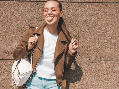 Yaz hipster ceket ve kot elbise giymiş güzel gülümseyen esmer model Portresi. Duvara yakın sokakta poz veren modaya uygun kız. Yuvarlak güneş gözlüğü komik ve pozitif kadın