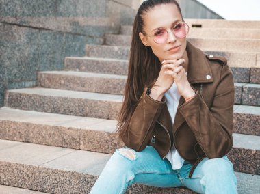 Yaz hipster ceket ve kot elbise giymiş güzel esmer model Portresi. Sokak arka planda merdivenlerde oturan trendy kız. Yuvarlak güneş gözlüğü komik ve pozitif kadın