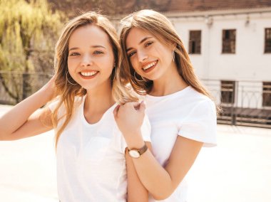 Moda yaz beyaz t-shirt giysiler iki genç güzel sarışın gülümseyen hipster kız Portresi. Seksi kaygısız kadınlar sokak arka planda poz. Olumlu modeller eğleniyor. Sarılma
