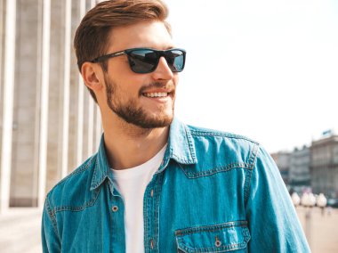 Yakışıklı gülümseyen şık hipster lumbersexual işadamı modeli portresi. Kot pantolon ceketi giymiş bir adam. Moda erkek güneş gözlüğü sokak arka planda poz