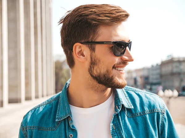 Yakışıklı gülümseyen şık hipster lumbersexual işadamı modeli portresi. Kot pantolon ceketi giymiş bir adam. Moda erkek güneş gözlüğü sokak arka planda poz