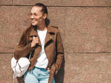 Yaz hipster ceket ve kot elbise giymiş güzel gülümseyen esmer model Portresi. Duvara yakın sokakta poz veren modaya uygun kız. Yuvarlak güneş gözlüğü komik ve pozitif kadın