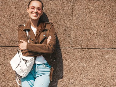 Yaz hipster ceket ve kot elbise giymiş güzel gülümseyen esmer model Portresi. Duvara yakın sokakta poz veren modaya uygun kız. Yuvarlak güneş gözlüğü komik ve pozitif kadın