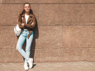 Yaz hipster ceket ve kot elbise giymiş güzel gülümseyen esmer model Portresi. Duvara yakın sokakta poz veren modaya uygun kız. Yuvarlak güneş gözlüğü komik ve pozitif kadın