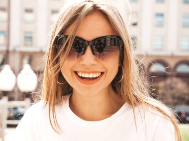 Yaz hipster giysileri giymiş güzel gülümseyen sarışın model portresi. Sokak arka planda poz veren modaya uygun bir kız. Güneş gözlüğü komik ve pozitif kadın