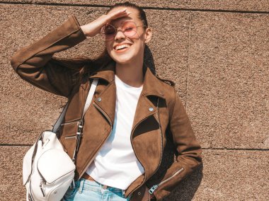 Yaz hipster ceket ve kot elbise giymiş güzel gülümseyen esmer model Portresi. Duvara yakın sokakta poz veren modaya uygun kız. Yuvarlak güneş gözlüğü komik ve pozitif kadın
