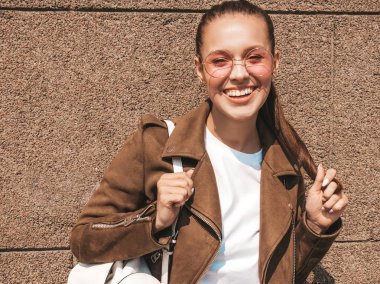 Yaz hipster ceket ve kot elbise giymiş güzel gülümseyen esmer model Portresi. Duvara yakın sokakta poz veren modaya uygun kız. Yuvarlak güneş gözlüğü komik ve pozitif kadın