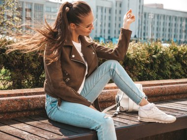 Yaz hipster ceket ve kot elbise giymiş güzel esmer model Portresi. Sokak arka planda bankta oturan trendy kız. Yuvarlak güneş gözlüğü komik ve pozitif kadın