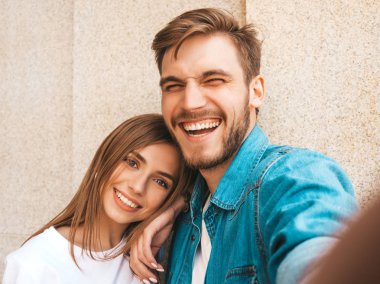 Gülümseyen güzel kız ve rahat yazlık giysiler onun yakışıklı erkek arkadaşı. Mutlu aile akıllı telefon kamerasında selfie selfie kendi portresini çekiyor. Sokak arka planda eğlenmek 