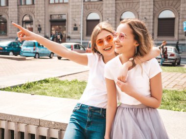 Beyaz hipster giysiler ivedi likle yaz güneşli günde iki genç şık hippi esmer ve sarışın kadın modellerin moda portresi sokak arka planda poz. Dükkan satışlarını işaret eden kızlar