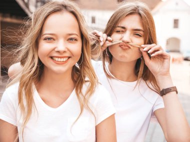 Moda yaz beyaz t-shirt giysiler iki genç güzel sarışın gülümseyen hipster kız Portresi. Sokakta poz veren seksi kaygısız kadınlar. Olumlu modeller eğleniyor. Saç ile bıyık yapma