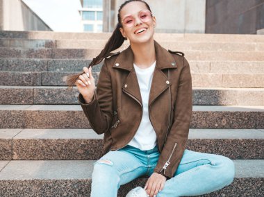 Yaz hipster ceket ve kot elbise giymiş güzel gülümseyen esmer model Portresi. Sokak arka planda merdivenlerde oturan trendy kız. Yuvarlak güneş gözlüğü komik ve pozitif kadın