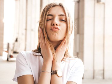 Yaz hipster giysileri giymiş güzel sarışın model portresi. Sokak arka planda poz veren modaya uygun bir kız. Komik ve pozitif kadın eğleniyor. Ördek surat yapar