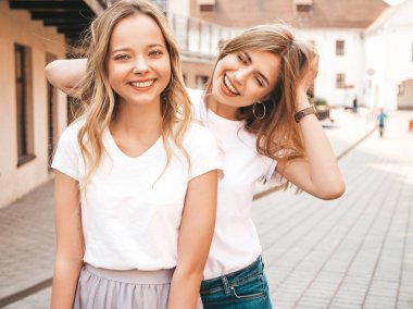 Moda yaz beyaz t-shirt giysiler iki genç güzel sarışın gülümseyen hipster kız Portresi. Seksi kaygısız kadınlar sokak arka planda poz. Olumlu modeller eğleniyor. Sarılma