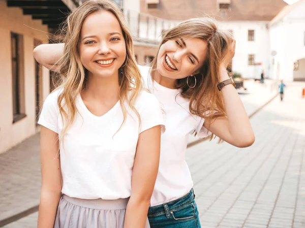 Moda yaz beyaz t-shirt giysiler iki genç güzel sarışın gülümseyen hipster kız Portresi. Seksi kaygısız kadınlar sokak arka planda poz. Olumlu modeller eğleniyor. Sarılma