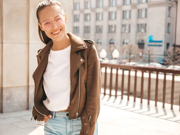 Portrait of beautiful smiling brunette model dressed in summer hipster jacket clothes. Trendy girl posing in the street background. Funny and positive woman in round sunglasses