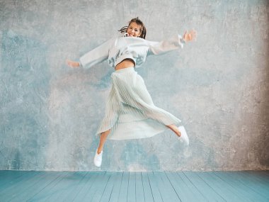 Güzel sevimli gülümseyen model atlama. Yaz hipster kapüşonlu ve etek kız. Model eğlenmek ve stüdyoda gri duvar yakınında deli gidiyor. El kaldırma