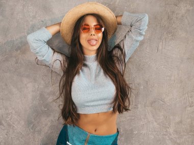 Kameraya bakan genç güzel kadının portresi. Rahat yaz tulum giysi ve şapka Trendy kız. Komik ve pozitif kadın stüdyoda gri duvar yakınında poz