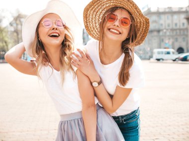 Moda yaz beyaz t-shirt giysiler iki genç güzel sarışın gülümseyen hipster kız Portresi. Seksi kaygısız kadınlar sokak arka planda poz. Güneş gözlüğü ve şapka ile eğlenen pozitif modeller