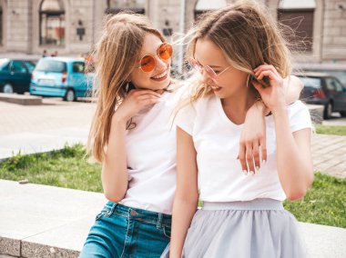 Moda yaz beyaz t-shirt giysiler iki genç güzel sarışın gülümseyen hipster kız Portresi. Seksi kaygısız kadınlar sokak arka planda poz. Güneş gözlüğü ile eğlenen pozitif modeller. Sarılma