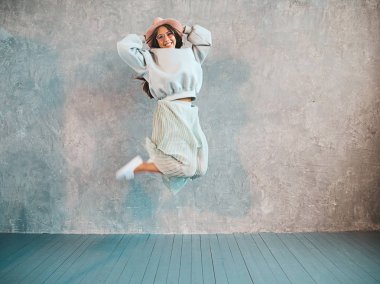 Güzel sevimli gülümseyen model atlama. Yaz hipster kapüşonlu ve etek kız. Model eğlenmek ve stüdyoda gri duvar yakınında deli gidiyor