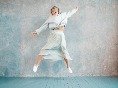 Güzel sevimli gülümseyen model atlama. Yaz hipster kapüşonlu ve etek kız. Model eğlenmek ve stüdyoda gri duvar yakınında deli gidiyor