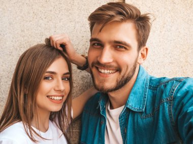 Gülümseyen güzel kız ve rahat yazlık giysiler onun yakışıklı erkek arkadaşı. Mutlu aile akıllı telefon kamerasında selfie selfie kendi portresini çekiyor. Sokak arka planda eğlenmek 
