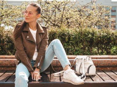 Yaz hipster ceket ve kot elbise giymiş güzel esmer model Portresi. Sokak arka planda bankta oturan trendy kız. Yuvarlak güneş gözlüğü komik ve pozitif kadın
