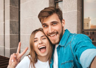Gülümseyen güzel kız ve rahat yazlık giysiler onun yakışıklı erkek arkadaşı. Mutlu aile akıllı telefon kamerasında selfie selfie kendi portresini çekiyor. Sokak arka planda eğlenmek 