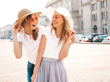 Moda yaz beyaz t-shirt giysiler iki genç güzel sarışın gülümseyen hipster kız Portresi. Seksi kaygısız kadınlar sokak arka planda poz. Güneş gözlüğü ve şapka ile eğlenen pozitif modeller