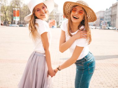 Moda yaz beyaz t-shirt giysiler iki genç güzel sarışın gülümseyen hipster kız Portresi. Seksi kaygısız kadınlar sokak arka planda poz. Birbirini tutan pozitif modeller