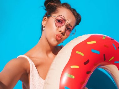 Güneş gözlüğü genç güzel seksi gülümseyen hipster kadın. Donut lilo şişme döşekli yazlık kıyafetler giyen kız deliriyordu. Mavi üzerine izole edilmiş komik bir model. Telefonda selfie selfie portre fotoğrafları çekmek