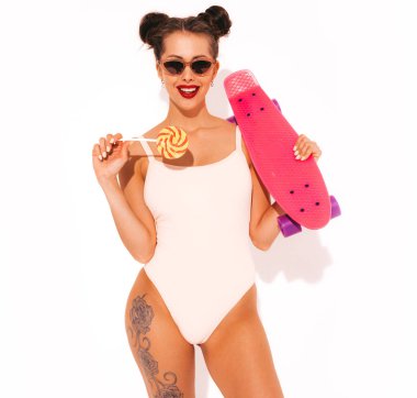 Güneş gözlüğü kırmızı dudaklar ile Genç güzel seksi gülümseyen hipster kadın. Yazlık mayo giyen kız. Pembe peni kaykay ile deli gidiyor, beyaz izole. İki boynuz. Şeker lolipop yeme