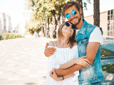 Gülümseyen güzel kız ve yakışıklı erkek arkadaşı. Gündelik yazlık elbiseli kadın ve kot elbiseli adam. Mutlu, neşeli bir aile. Kadın arka planda eğleniyor. Güneş gözlüklü çifte sarılıyor.