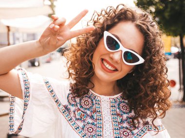 Yaz hipster beyaz elbise giymiş afro bukleler saç modeli ile güzel gülümseyen model. Seksi kaygısız kız sokakta poz. Trendy komik ve pozitif kadın güneş gözlüğü eğlenmek. Barış işaretini gösterir