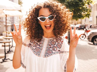 Yaz hipster beyaz elbise giymiş afro bukleler saç modeli ile güzel gülümseyen model. Seksi kaygısız kız sokakta poz. Trendy komik ve pozitif kadın güneş gözlüğü eğlenmek. Barış işaretini gösterir