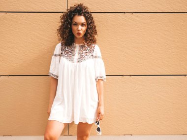 Yaz hipster beyaz elbise giymiş afro bukleler saç modeli ile güzel gülümseyen model. Seksi kaygısız kız sarı duvara yakın sokakta poz. Komik ve pozitif kadın eğleniyor. Ördek surat yapar