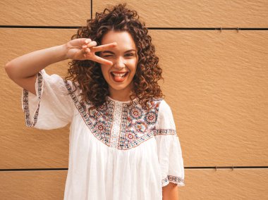 Yaz hipster beyaz elbise giymiş afro bukleler saç modeli ile güzel gülümseyen model. Seksi kaygısız kız sarı duvara yakın sokakta poz. Komik ve pozitif kadın eğleniyor. Dili gösterir