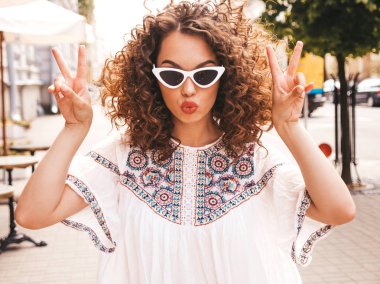 Yaz hipster beyaz elbise giymiş afro bukleler saç modeli ile güzel gülümseyen model. Seksi kaygısız kız sokakta poz. Trendy komik ve pozitif kadın güneş gözlüğü eğlenmek. Barış işaretini gösterir