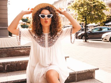 Yaz hipster beyaz elbise giymiş afro bukleler saç modeli ile güzel gülümseyen model. Seksi kaygısız kız sokakta poz. Trendy ve pozitif kadın güneş gözlüğü eğlenmek. Şapkalı ördek suratı yapar