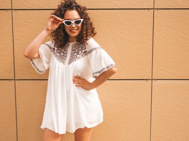 Yaz hipster beyaz elbise giymiş afro bukleler saç modeli ile güzel gülümseyen model. Seksi kaygısız kız güneş gözlüğü sarı duvar a yakın sokakta poz. Olumlu kadın eğleniyor